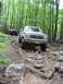 1991 Ford Bronco - Two off-road vehicles navigate a rocky, muddy path through a dense forest during an event.