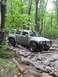 1991 Ford Bronco - A silver SUV tackles a challenging off-road course through a dense forest.