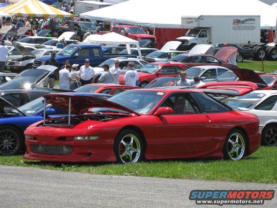 Red 1993 Ford Probe coupe with hood open, parked on grass at a car show
