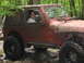 1991 Ford Bronco - A woman drives a red Jeep Wrangler through a rocky stream in a wooded area.