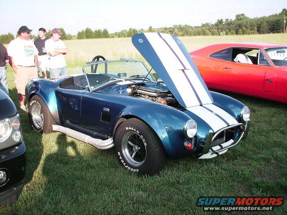 Blue convertible with white stripes, hood open, side pipes, and racing tires