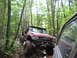 1991 Ford Bronco - A red off-road truck drives through a muddy forest path, with another vehicle partially visible on the right.