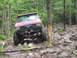 1991 Ford Bronco - This modified SUV navigates a challenging rocky and muddy path through a dense forest.
