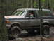 1991 Ford Bronco - A 1991 Ford Bronco navigates a challenging muddy trail in a forest setting.