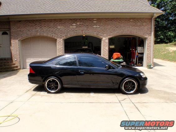 Black coupe side view parked in front of a brick garage