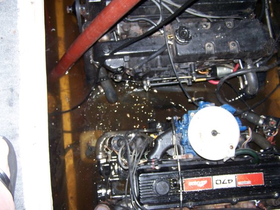 Boat engine with red hose and water on the floor. Red and white badge reads '470'