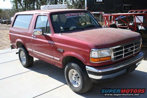 Red Ford Bronco parked outside, dust on hood. Sticker on windshield says 'EAGLE'S ON MOTORSPORT DESIGNS'