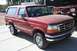 1989 Ford Bronco - This red Ford Bronco is parked on a concrete surface with a trailer and a buggy in the background.