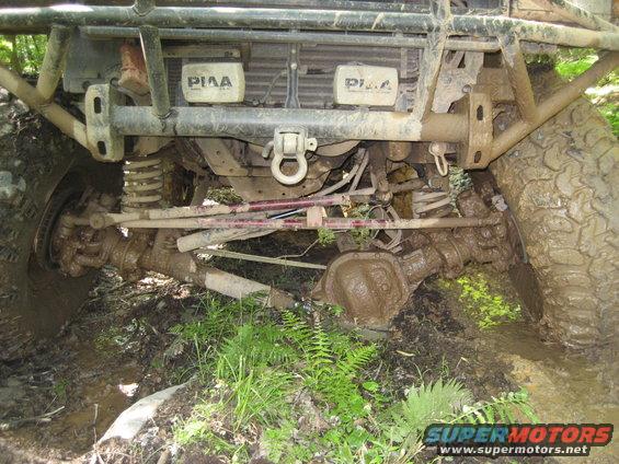 Off-road vehicle front axle, suspension, and tires covered in mud. PIAA lights visible