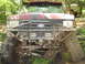 1991 Ford Bronco - This modified Ford Bronco is shown off-road, covered in mud, with another vehicle in the background.