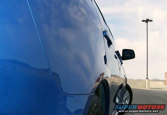 Side view of a blue van parked in a lot. A light pole is visible in the background