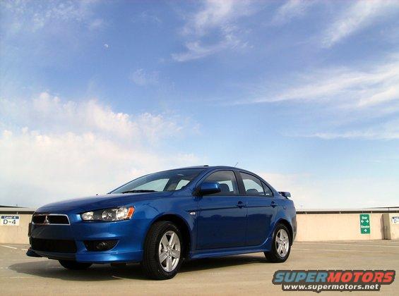 Blue 2009 Mitsubishi Lancer sedan parked on a concrete surface under a cloudy sky