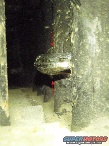 Tow point bolt with red arrows indicating its position, surrounded by dirt and grime
