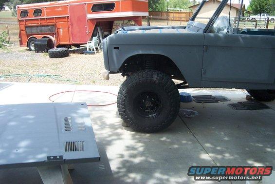 Gray SUV body with large tires, hood off, parked next to orange trailer