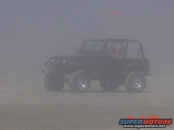 Black Jeep Wrangler with a red flag on a sandy terrain