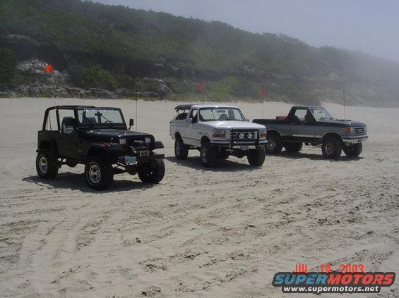 Black Jeep Wrangler, white Ford Bronco, and gray Ford pickup on a beach
