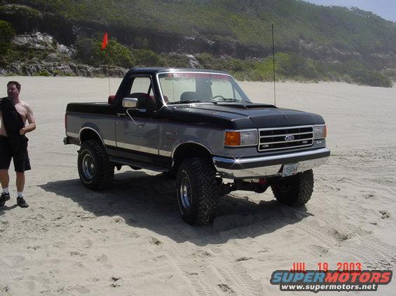 Ford Bronco parked on a sandy beach with a man standing nearby