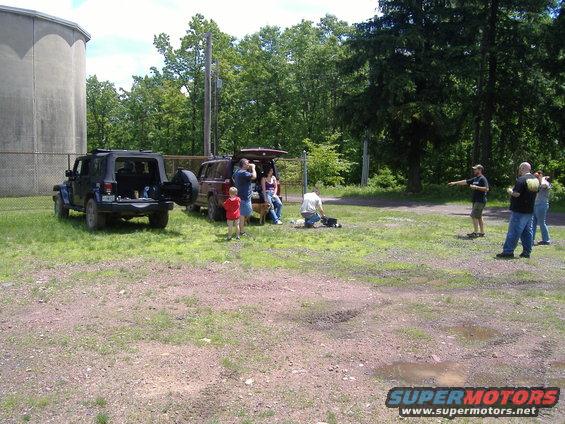 Jeep Wrangler and a red SUV parked in a grassy area with people around