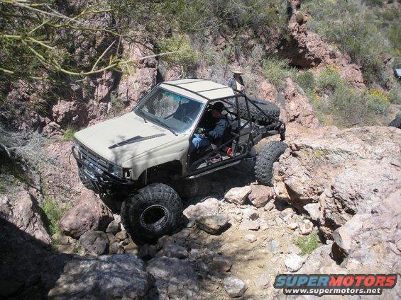 Modified Toyota pickup truck with roll cage and large tires navigating rocky terrain