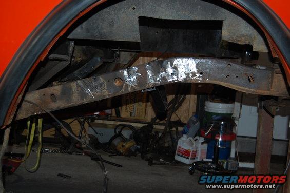 Close-up of rusty vehicle frame under orange body panel, with tools and containers in background