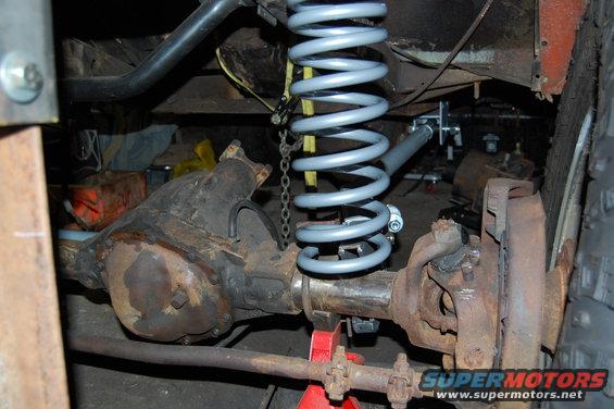 close-up of a vehicle's front axle, differential, and a new coil spring being installed