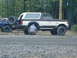1988 Ford Bronco - Two people work on the rear tire of a 1988 Ford Bronco parked next to another vehicle.