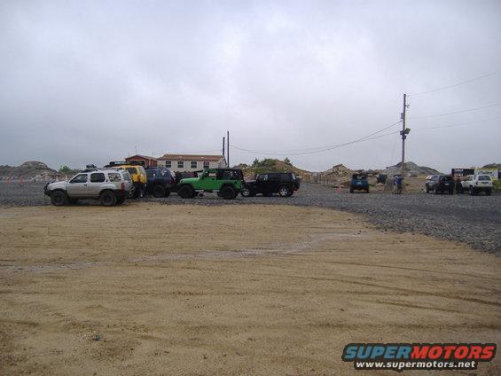 Several SUVs and Jeeps parked in an outdoor lot with buildings and rocky terrain in the background