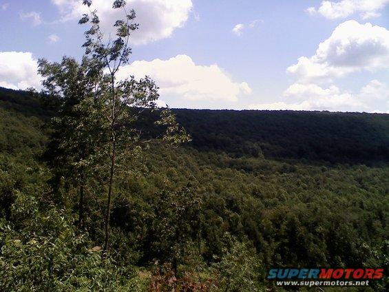 Wooded hillside under a cloudy sky with a "SUPERMOTORS" watermark