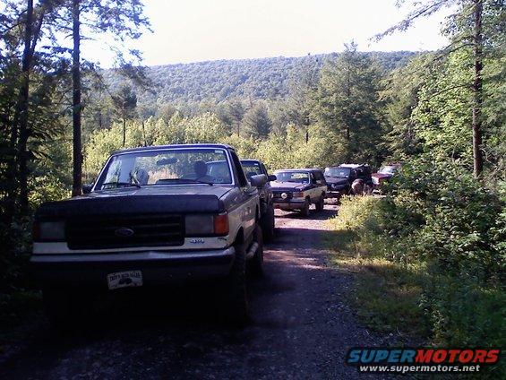 Ford truck in front, followed by several SUVs on a wooded dirt road
