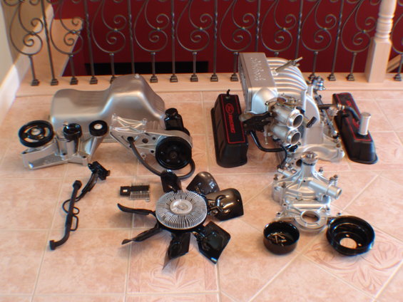 Engine parts including oil pan, intake manifold, valve covers, water pump, and fan laid out on a tiled floor
