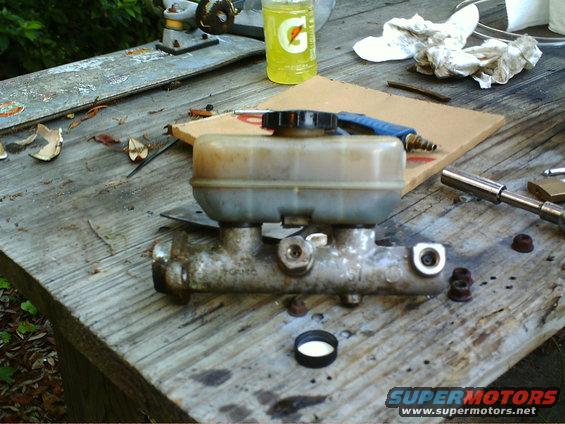 Brake master cylinder on a wooden surface with tools and a bottle of Gatorade nearby