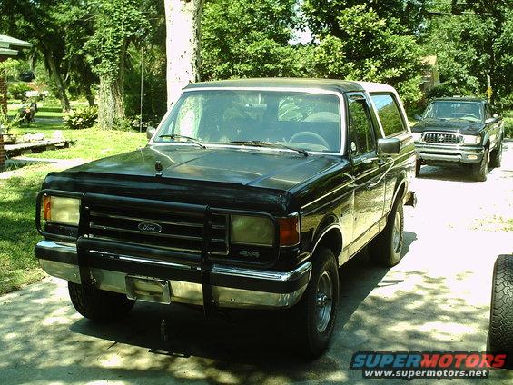 Black 1990 Ford Bronco parked in a driveway with a pickup truck behind it