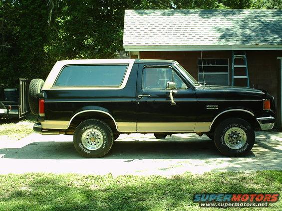 Black and tan Ford Bronco parked in driveway, spare tire on rear door
