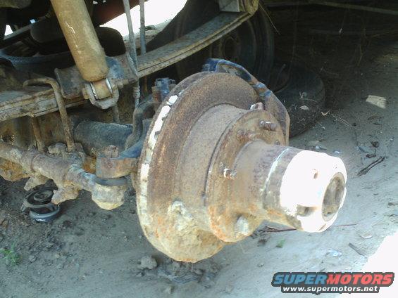 rusted front axle hub and brake assembly with leaf springs and shock absorber visible
