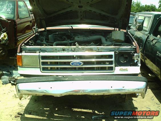 Front view of a 1987 Ford F-150 or Bronco with hood open, showing engine bay. Another truck is parked to the right