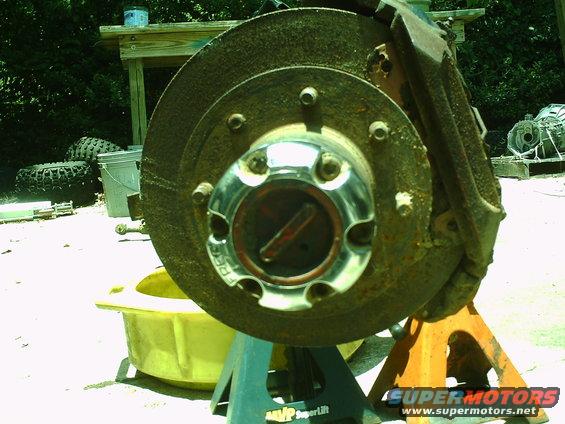 close-up of a rusty front wheel hub and brake rotor assembly on jack stands