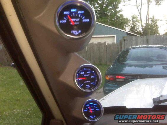 Interior view of a vehicle with three gauges, showing a green car in the background