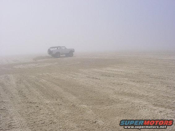 White SUV driving on a sandy surface in fog