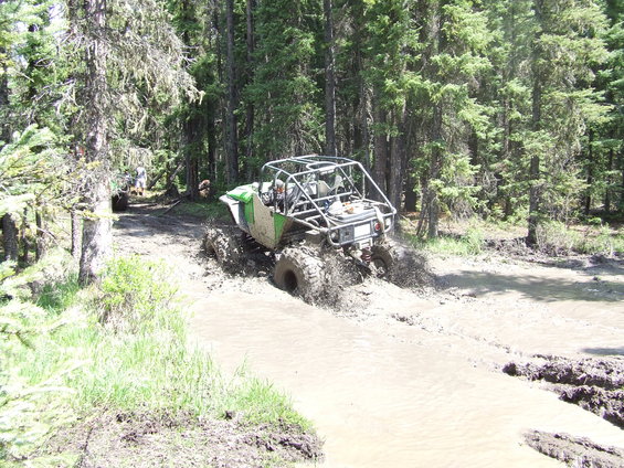 Off-road buggy with a roll cage driving through a muddy trail in a forest