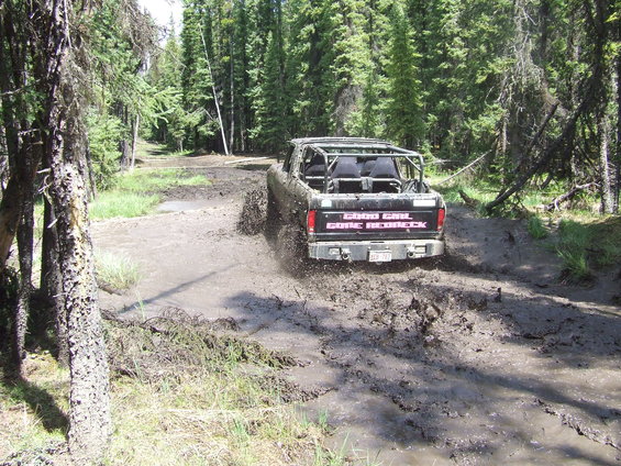 Black pickup truck with a roll cage driving through mud, splashing water