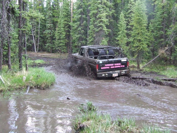 Black Ford Bronco with roll cage driving through mud, "GOOD GIRL GONE REDNECK" sticker on tailgate