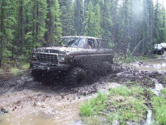 Ford Bronco stuck in mud, trees in background, another vehicle visible