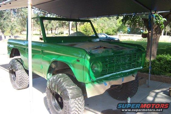 Green 1976 Ford Bronco with large tires, undergoing paintwork under a canopy