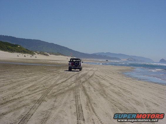 Black 1995 Jeep Wrangler driving on a beach, rear view