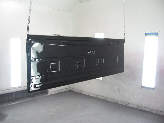 Black Ford tailgate hanging from chains in a paint booth. The word FORD is embossed on it