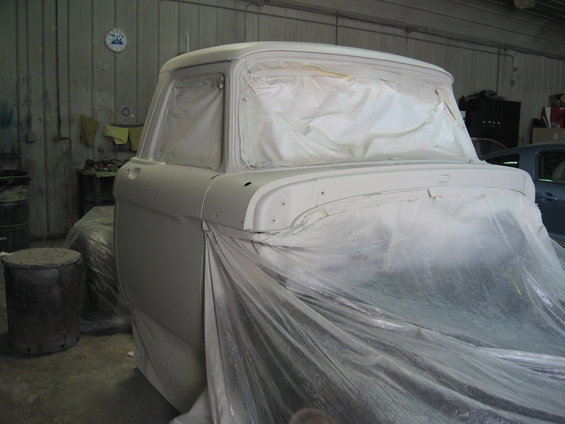 Light gray primer-covered truck cab, covered in plastic sheeting, viewed from the rear three-quarter angle