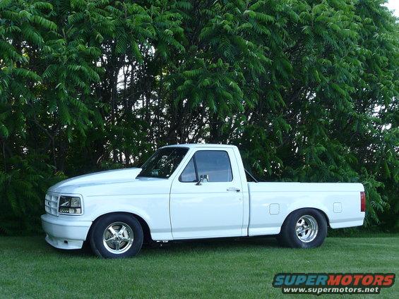 White pickup truck with a custom hood and chrome wheels parked on grass