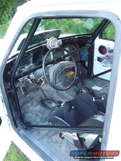 Interior of a white truck with roll cage, racing seat, and tachometer