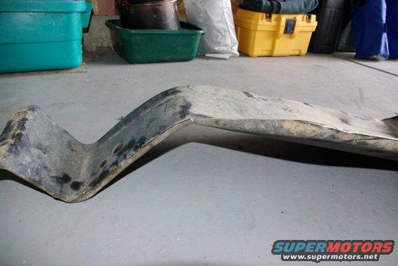 Bent metal skid plate on concrete floor, with storage bins and toolboxes in background