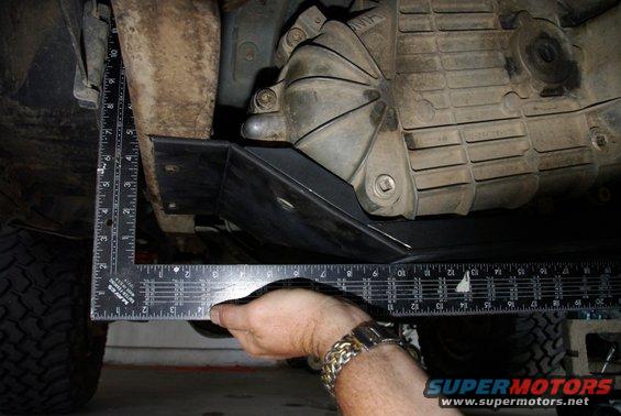 hand holding square ruler measuring under vehicle's transfer case skid plate